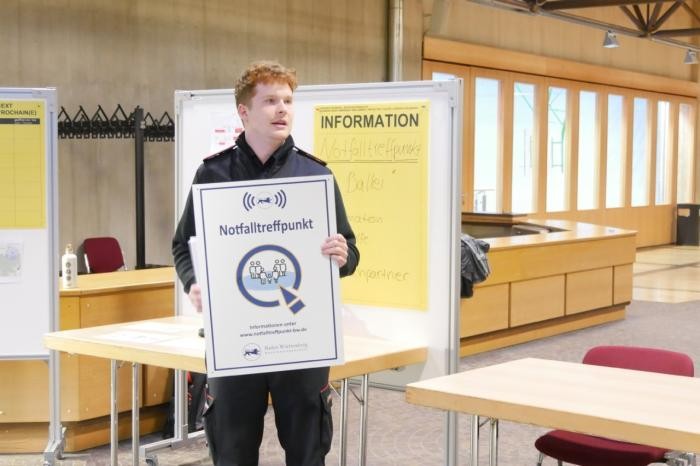 Projektbeauftragter Tim Zartmann hält im Ballei-Foyer das Schild "Notfalltraffpunkt" in Händen.