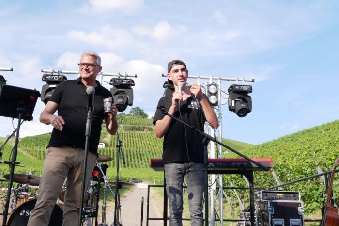 OB Steffen Hertwig und Jungwinzer Daniel Bauer stehen auf der Bühne mit dem Scheuerberg im Hintergrund.  