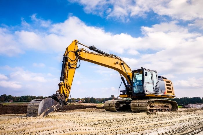 Ein Bagger steht auf einer Baustelle auf einem sandigen Untergrund.