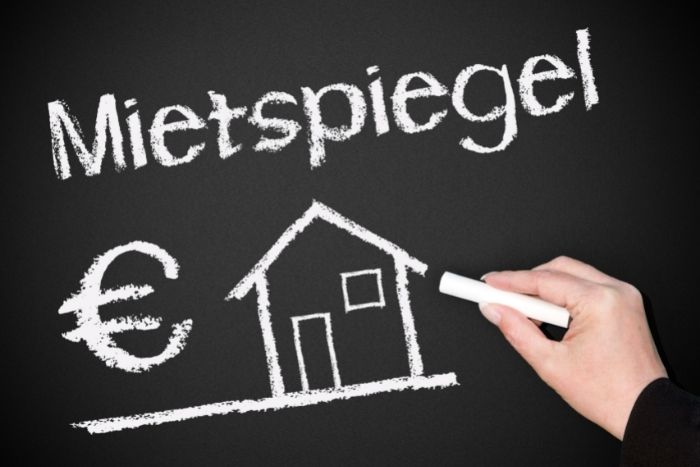 Foto: Adobe Stock Eine Hand schreibt mit Tafelkreide "Mietspiegel" auf einen schwarzen Hintergrund. Darunter sind ein €-Symbol und ein Haus abgebildet.