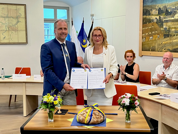 Unterzeichnung des Partnerschaftsvertrags zwischen Budakesi und Zschopau Zwei Personen im Vordergrund halten zusammen zwei Urkunden in die Kamera. Zwei Personen im Hintergrund klatschen in die Hände.