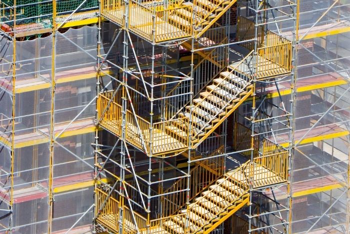 Foto: Adobe Stock. Ein gelbes Gerüst ist um ein Gebäude herum gebaut.