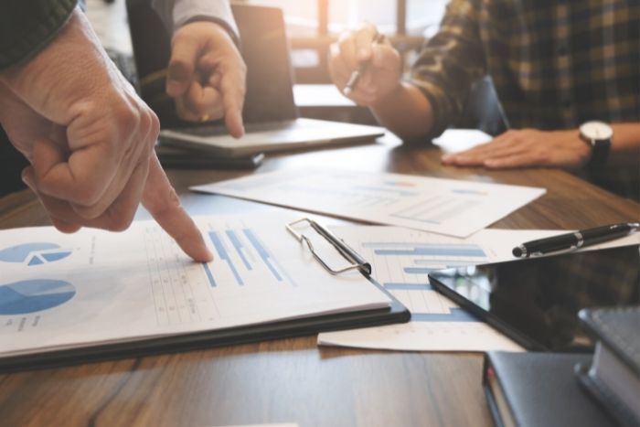 Foto: Adobe Stock Personen stehen an einem Tisch und zeigen auf Unterlagen. Eine Person hält einen Stift.